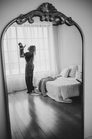Black and white reflections in ornate mirror show silhouettes in bright bedroom.