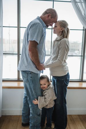 Family members embrace in a bright sunlit room with large windows and wooden floors.