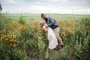 A romantic embrace between a couple in a field of bright orange wildflowers on a cloudy day.