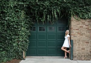 White dress swirling against ivy-covered garage door with green paint and brick wall.