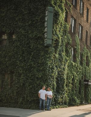 Couple standing next to an ivy-covered brick wall on a sunny day.
