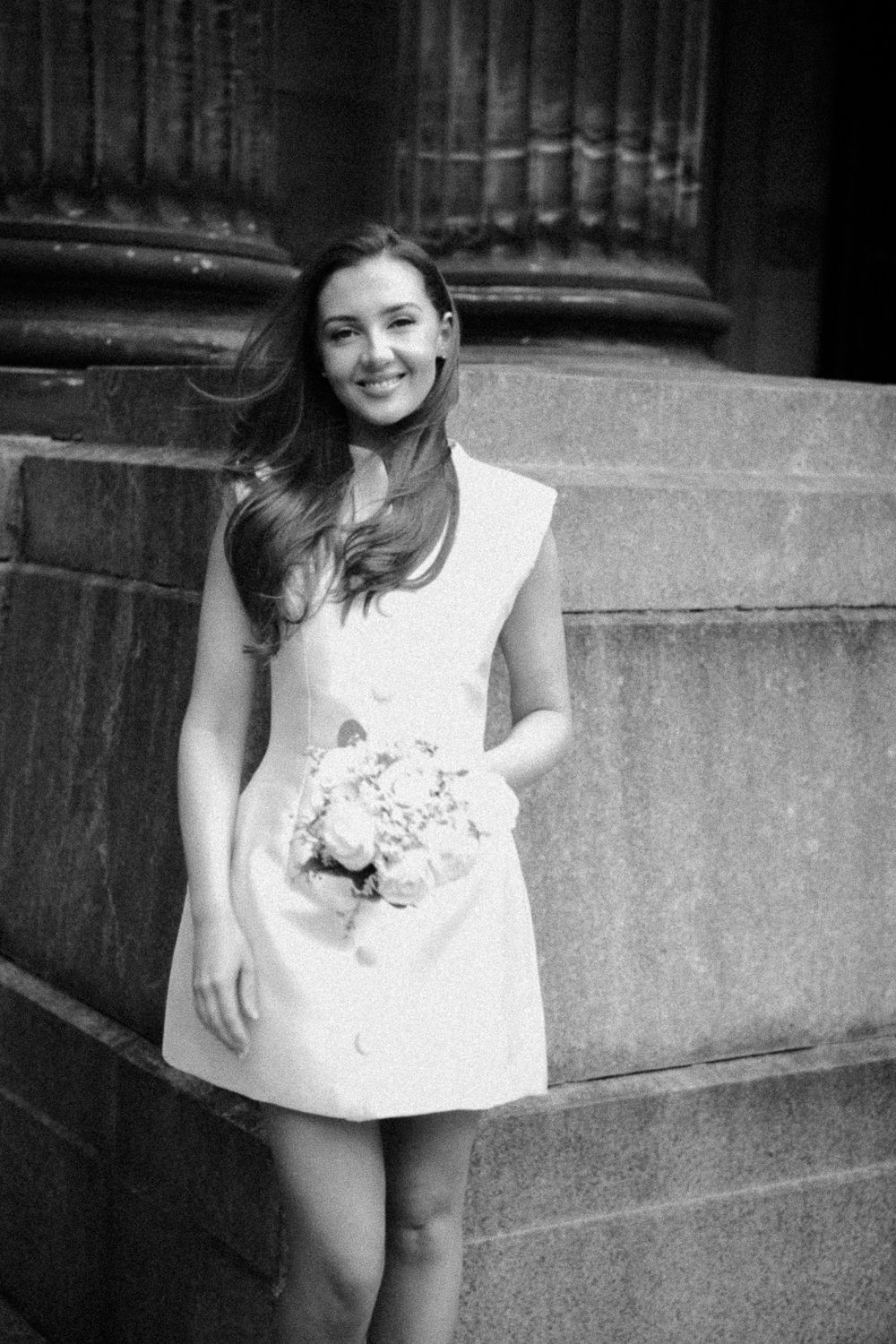 Portrait of a beautiful bride in black and white, the bride is standing in front of a stone column in front of a huge building.