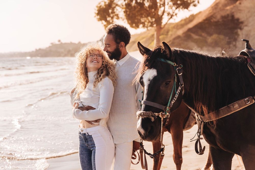 A couple shares a romantic moment on horseback during an outdoor photoshoot.