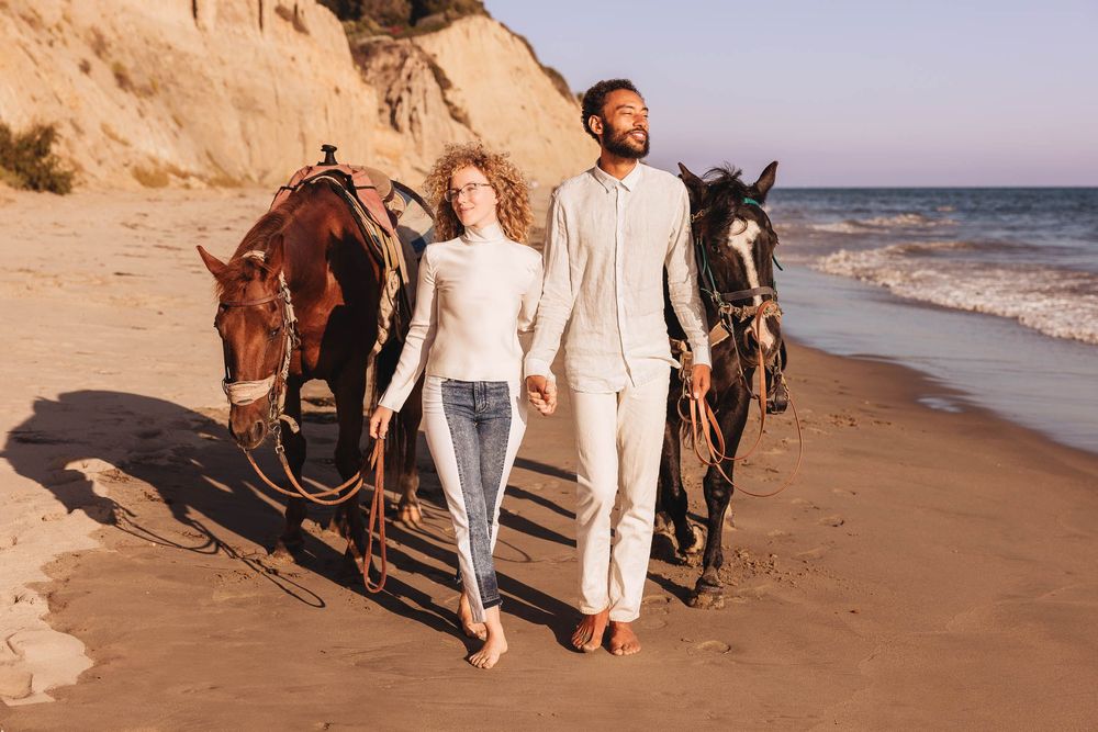 Romantic horseback riding scene on a beach with dramatic coastal cliffs and ocean waves at sunset.
