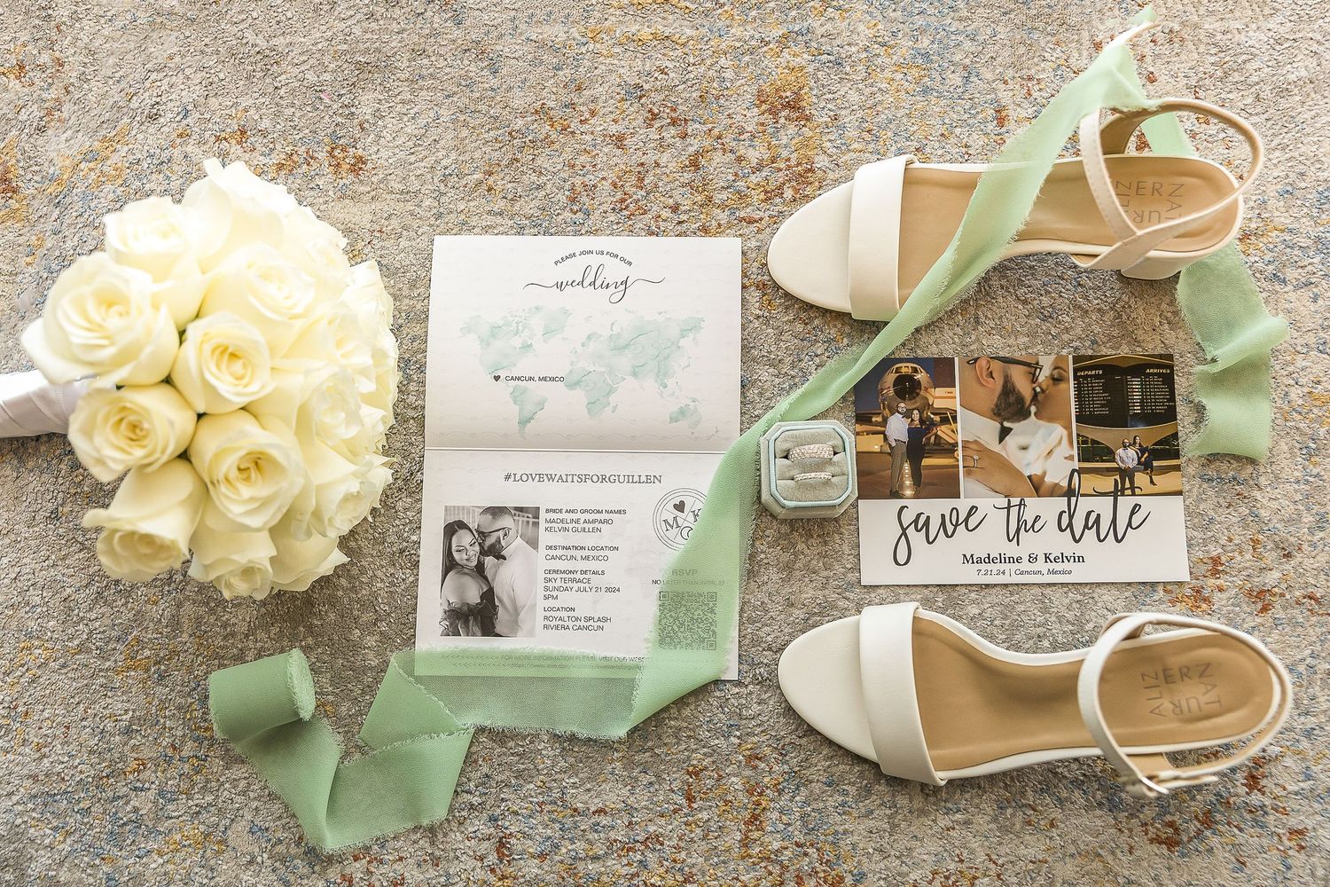 Wedding details including white roses, invitation and mint green ribbon next to elegant bridal shoes on stone surface.