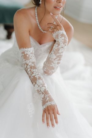 Bride in white ballgown wearing elegant lace gloves and pearl necklace, posing gracefully on her wedding day.