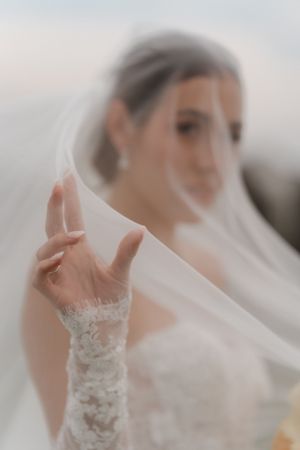 Artistic close-up of bride\u2019s lace gloved hand holding flowing veil with soft blurred background.