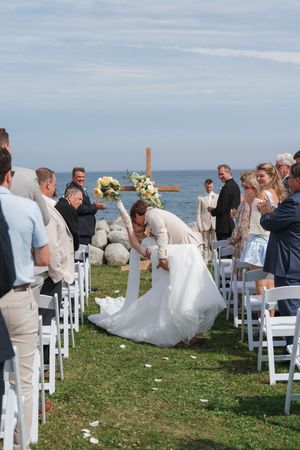 Bride and groom share a romantic moment during an outdoor beach wedding ceremony with white chairs and ocean backdrop.