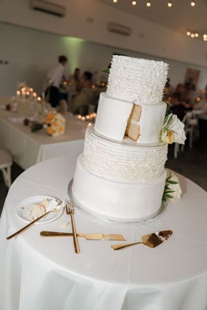 Four-tier white wedding cake with ruffled texture and floral accents on a draped table.