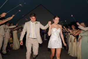 Newlyweds walk through sparkler exit tunnel with wedding guests at night outdoor reception celebration.