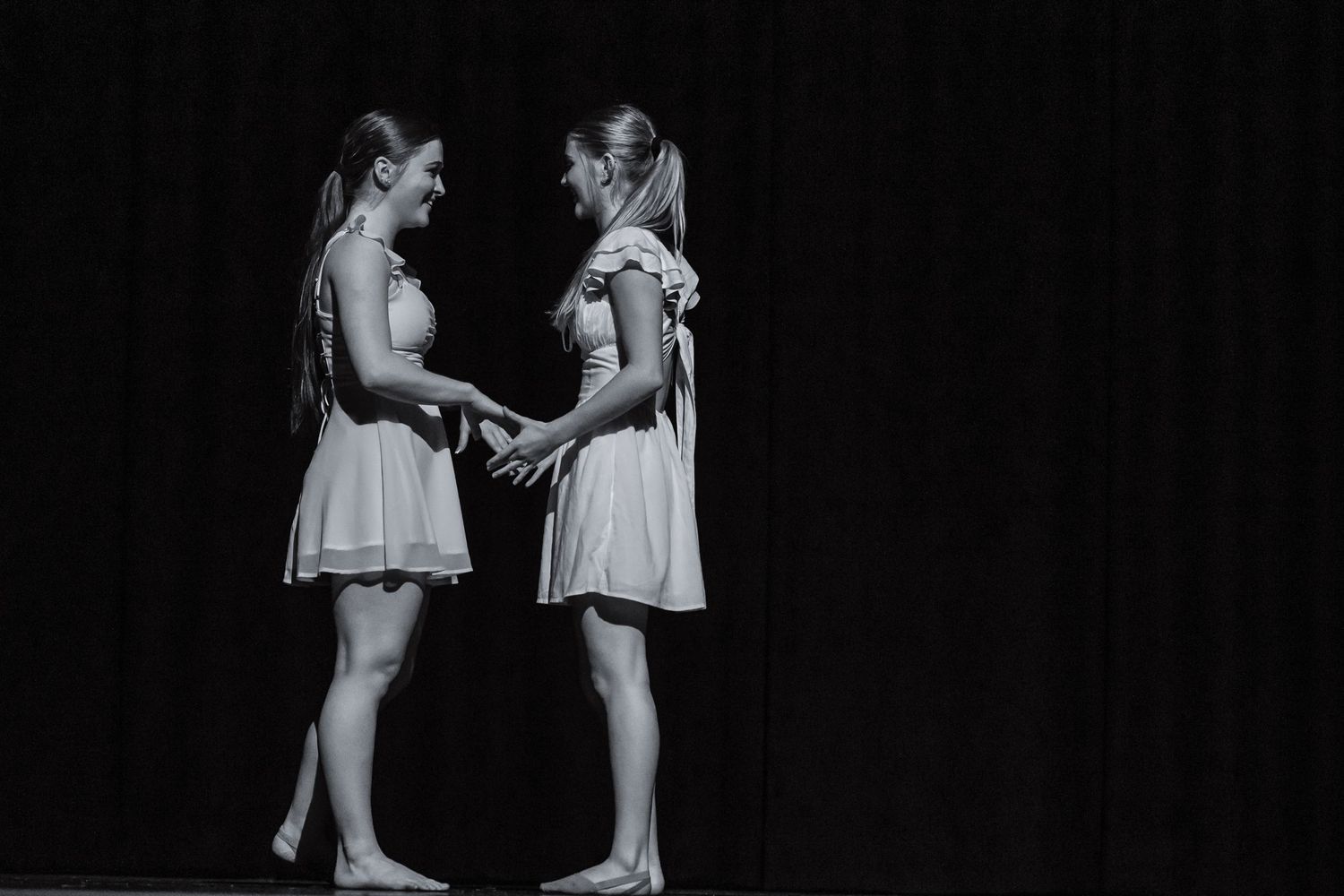Modern dance group in white shirts creates artistic formation on folding chairs.