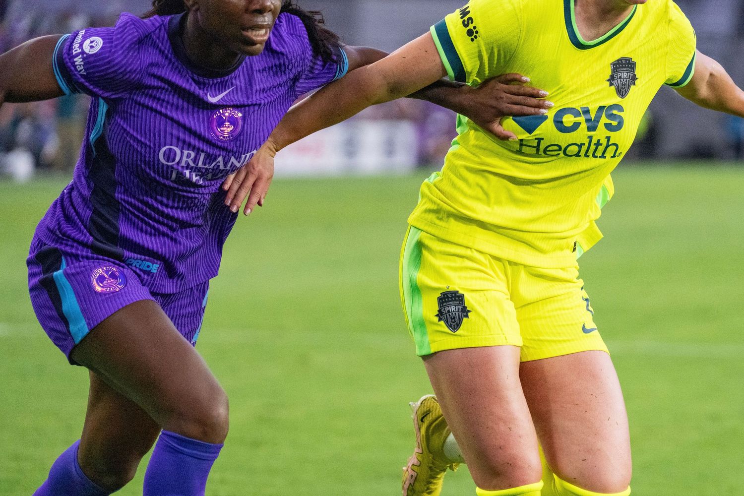 Two female soccer players compete for the ball, one in purple Orlando kit and one in yellow CVS Health sponsored jersey.