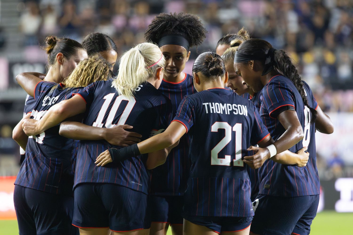 Soccer team huddles together in navy blue uniforms during match.