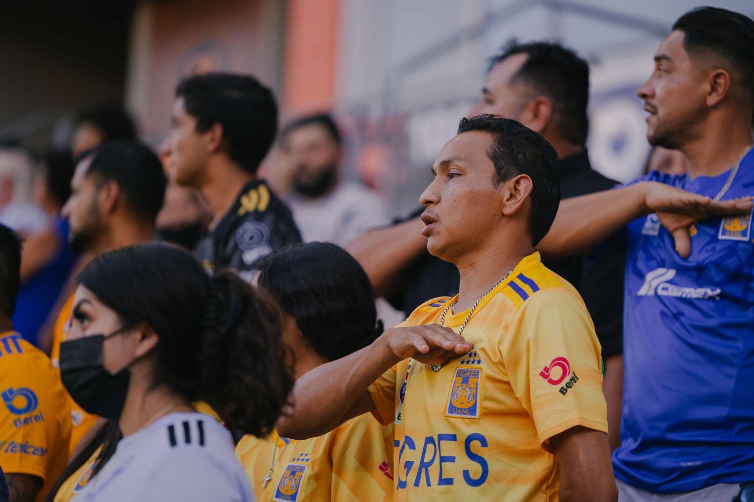 Soccer fans in yellow jerseys watch intently from stadium seats during an intense match.
