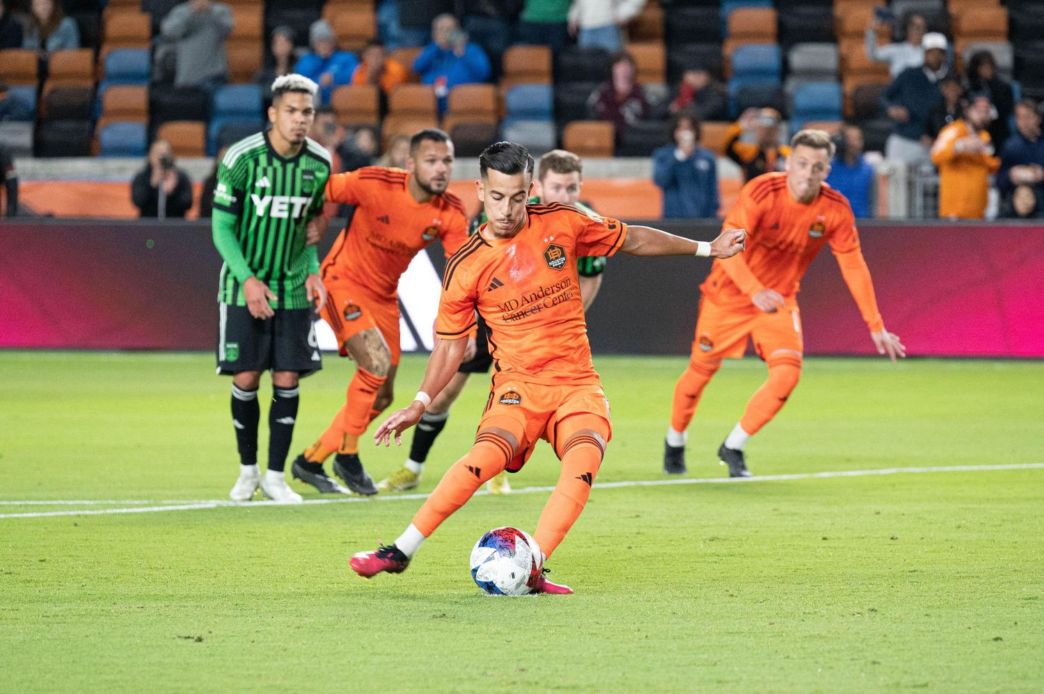 Soccer players in orange jerseys running across a stadium field during a match.