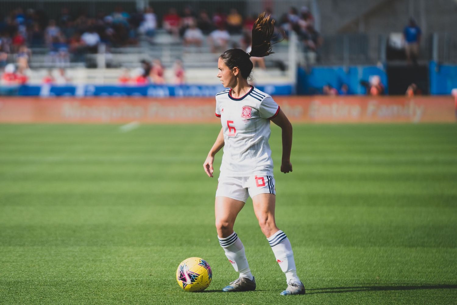 Soccer player in white uniform dribbles ball across green grass field during competitive match.