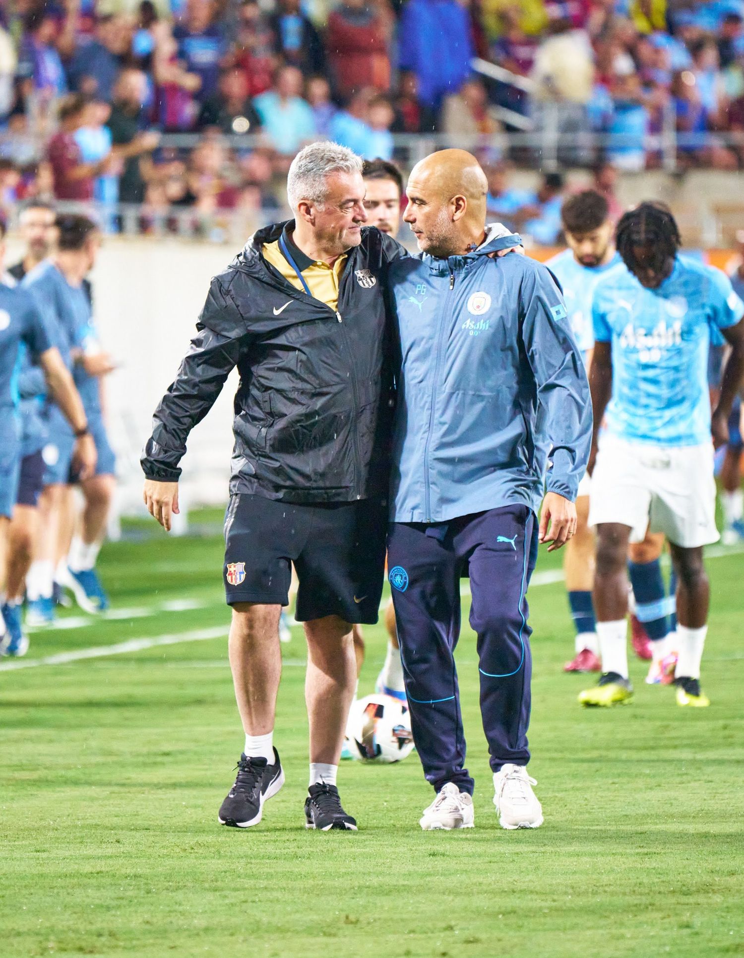 Soccer coaches walk across a field during warmups before a match.