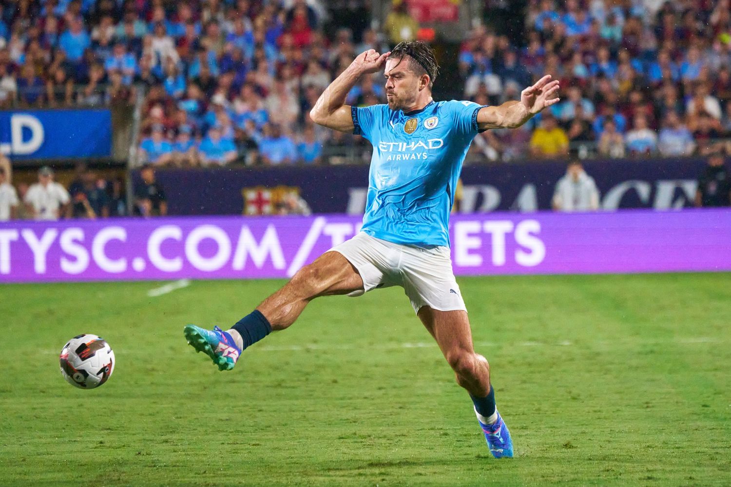 Soccer player in light blue jersey takes a shot during intense match action with crowd in background.
