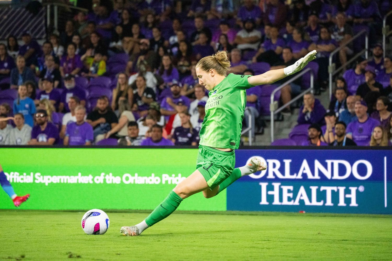 Goalkeeper in green uniform making diving save during soccer match.