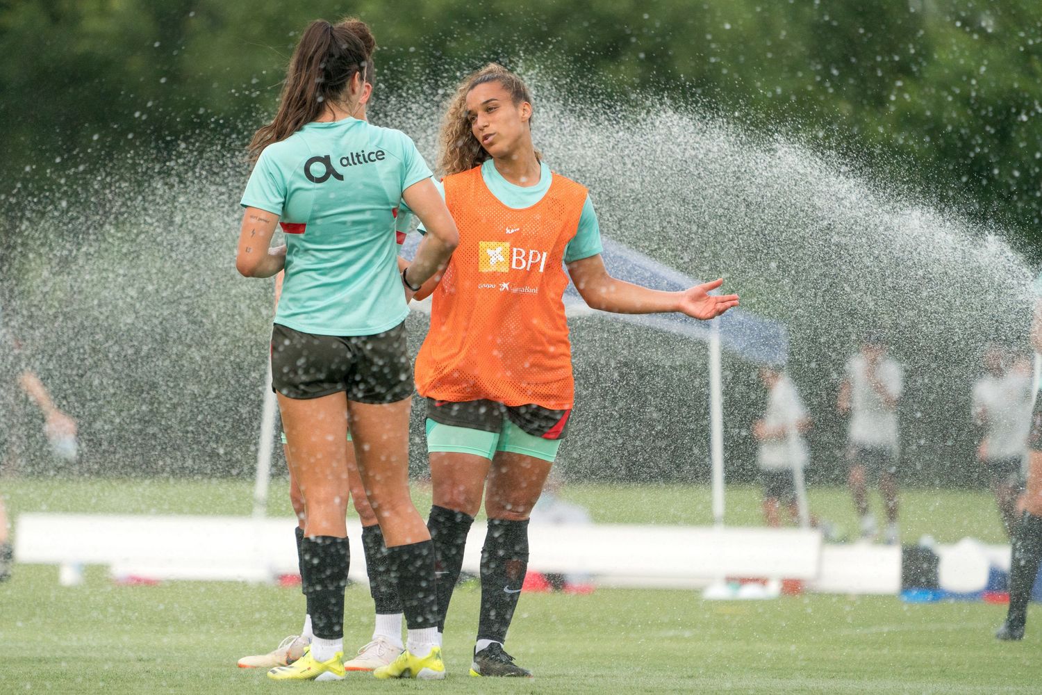 Soccer players get sprayed with water during a hot training session on the field.