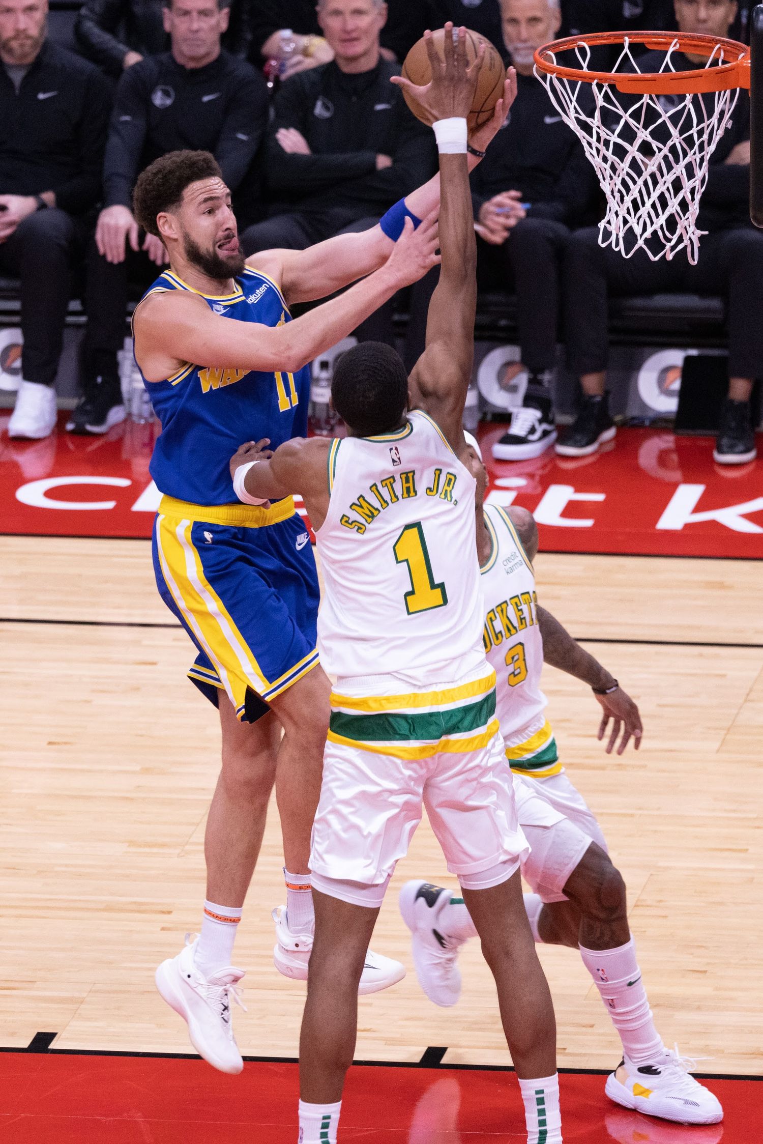 Basketball players battle for position during an intense game on a red court.