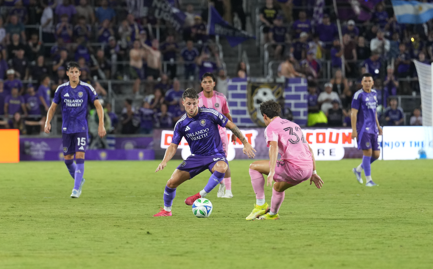 Soccer match in progress with players in purple uniforms on a stadium field.