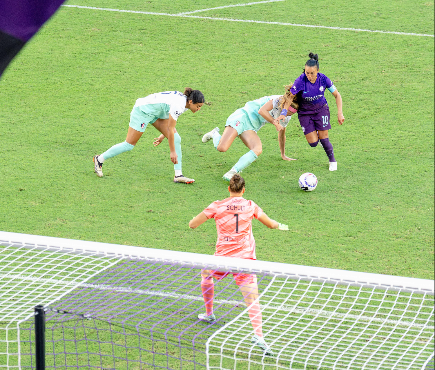 Soccer match action showing players near the goal net on a green field.