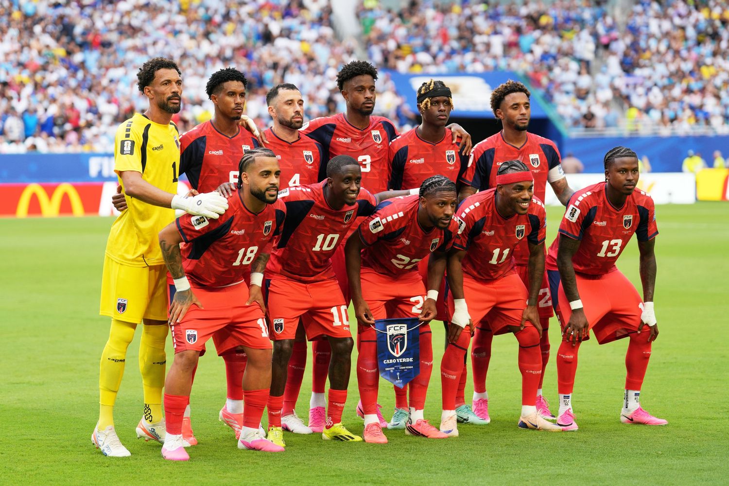 Haiti national soccer team posing for a group photo in red uniforms before a match at a sunny stadium.