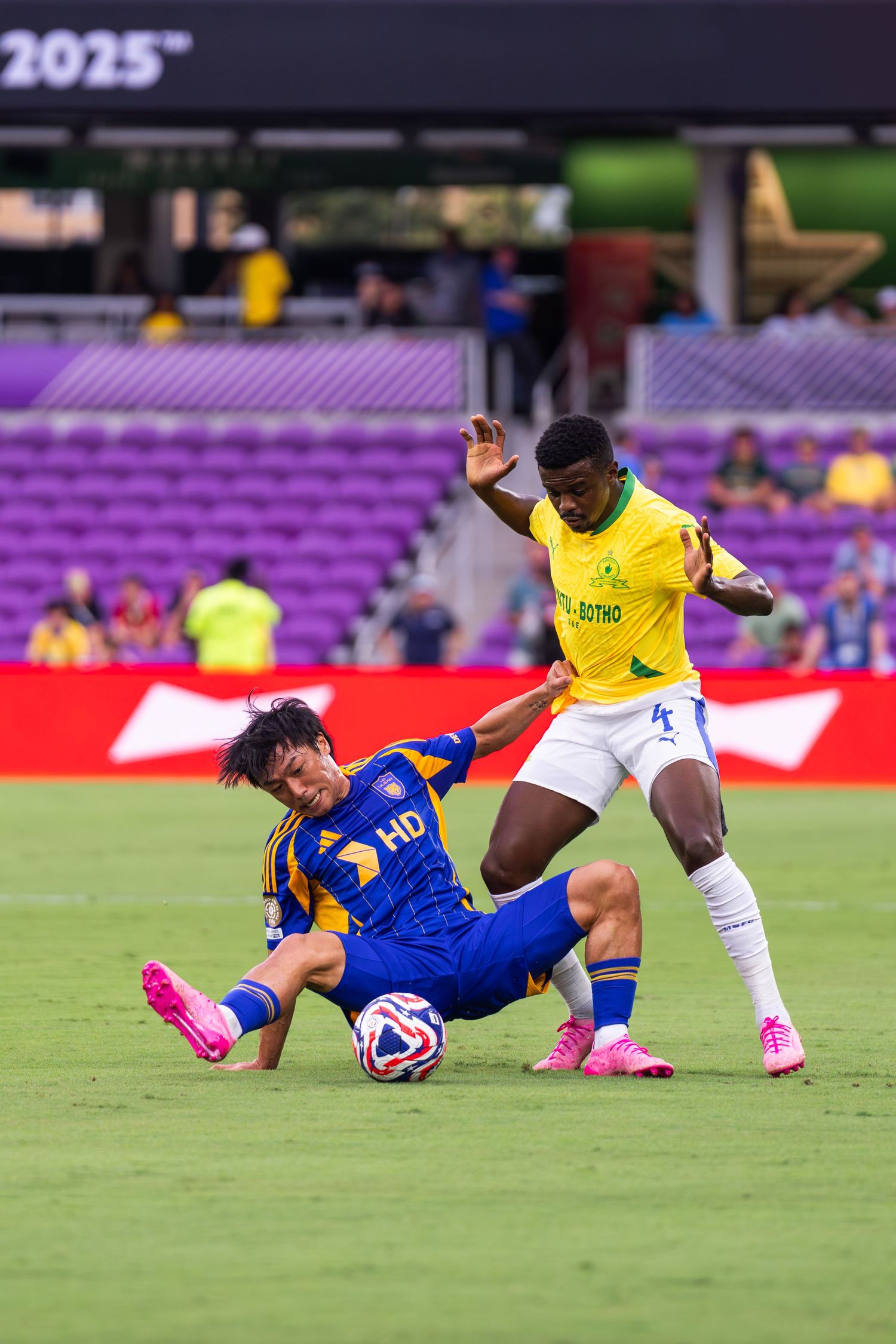 Soccer players collide during a tackle on a purple-lit stadium field.