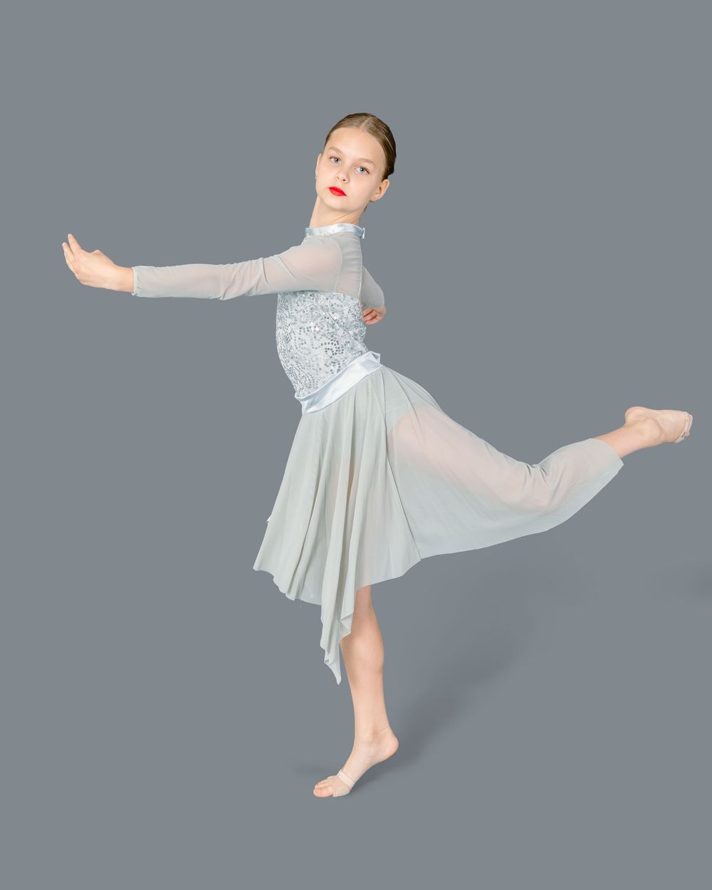 Dancer in white flowing dress performs an arabesque pose against a gray background.