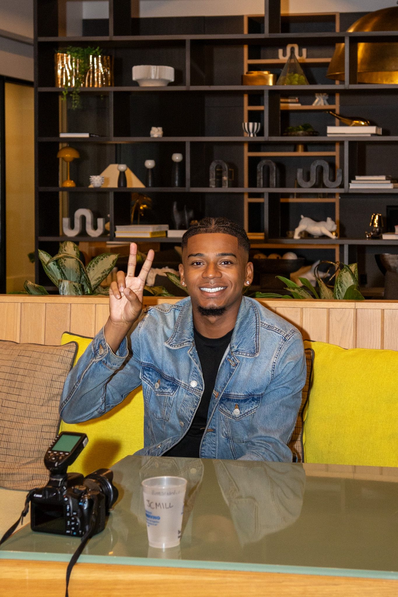 Casual portrait of person making peace sign while sitting at table with camera and drinks.