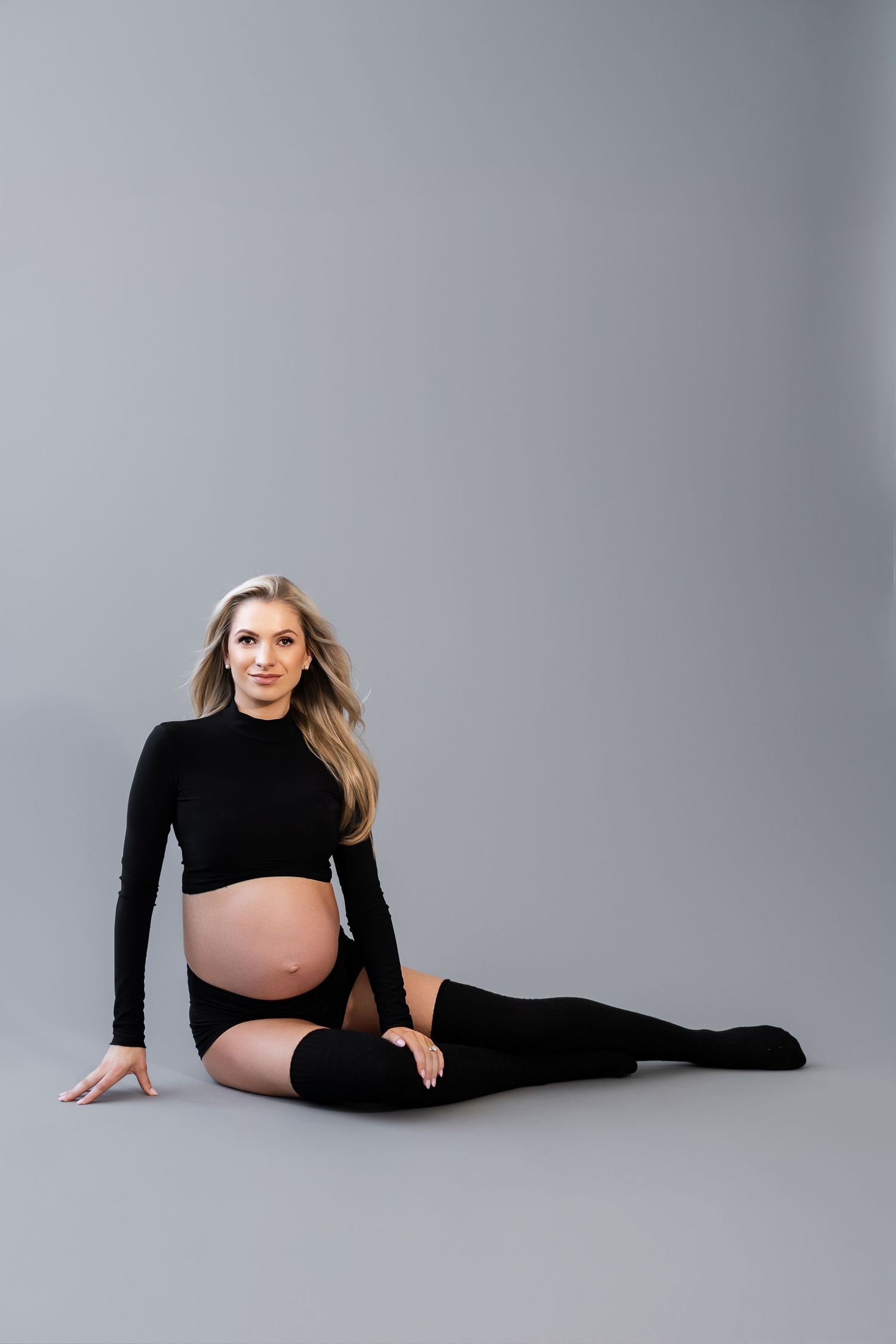 Maternity photo of an expectant mother in black athletic wear posed on gray backdrop.