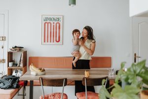 Two people stand on an orange mid-century sofa in a modern living room with minimalist decor and plants.