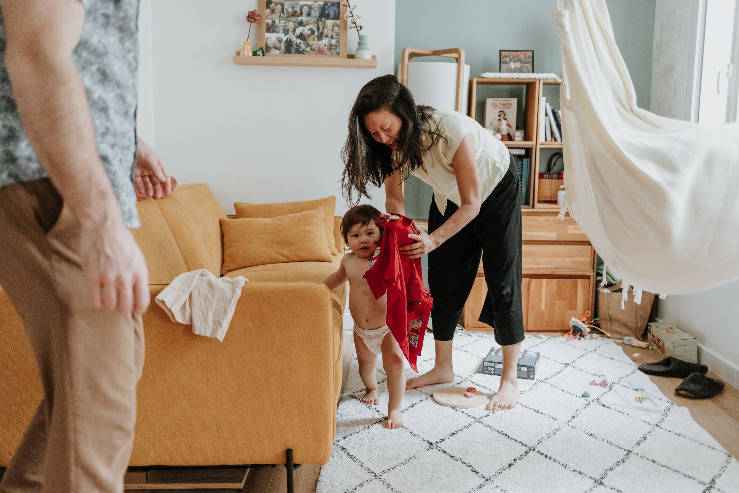 A family plays and laughs together on a patterned rug near their mustard yellow couch in a bright living room.