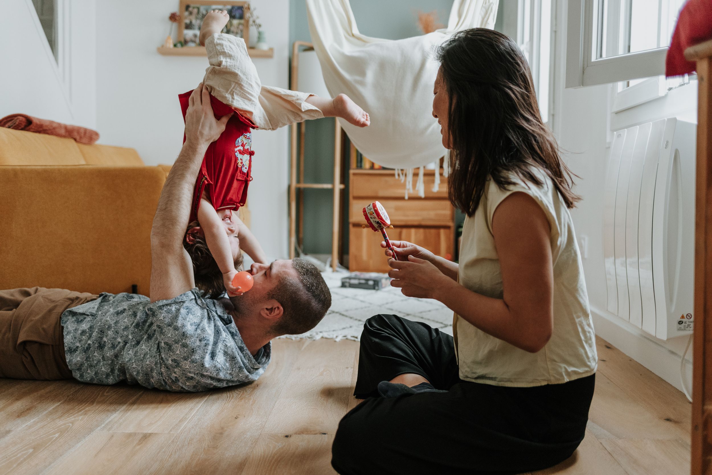 Two people play together on a hardwood floor, throwing pillows and enjoying a playful moment at home.