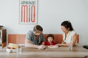 Young family gathered at dining table with orange wall art having relaxed morning time together at home.