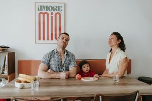 A family sits together laughing at a wooden table in a restaurant with a vintage orange sign on the wall.