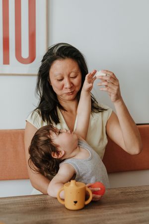 A tender moment between a parent and child during mealtime with a teapot and fruit on the wooden table.