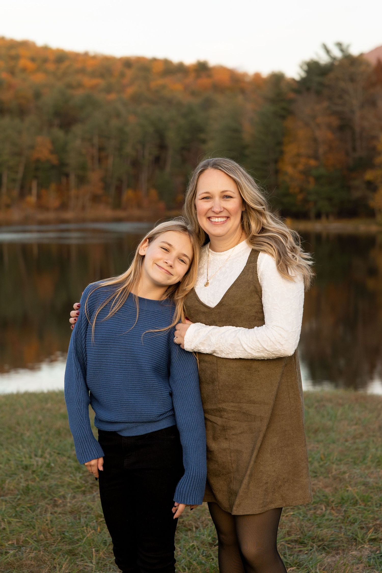 Two friends share a joyful moment together by a scenic autumn lake with colorful fall foliage in the background.