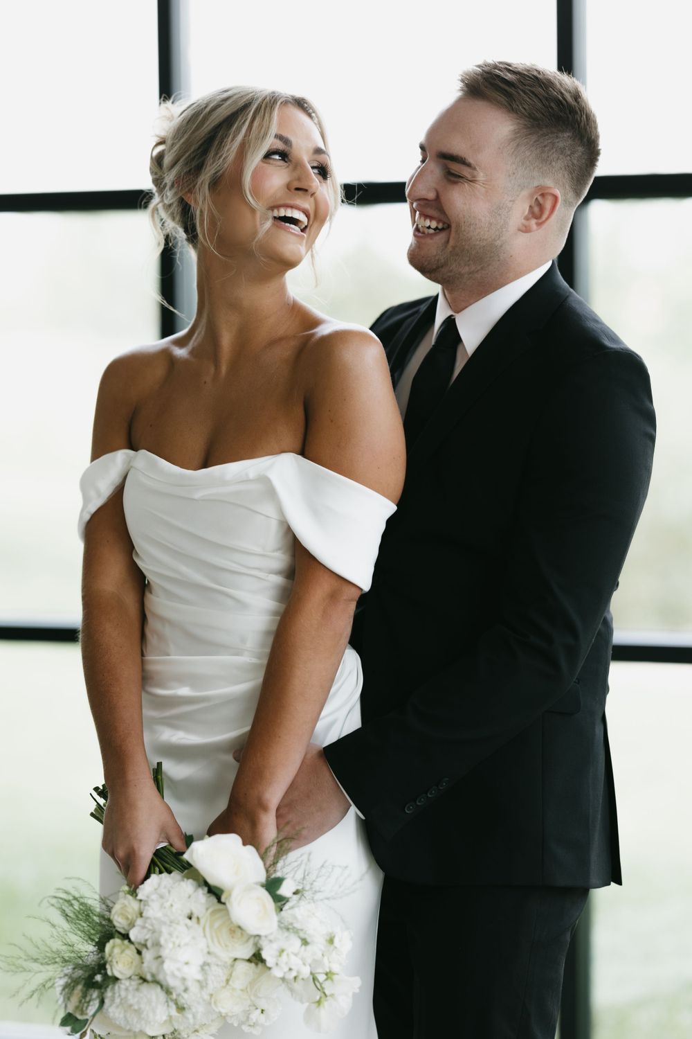 Joyful couple shares a candid laughing moment in formal wedding attire.