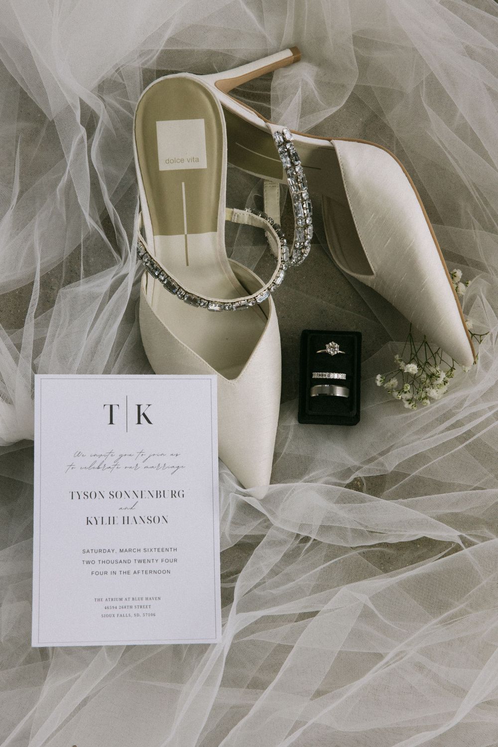 Wedding details including white heels, rings, invitation, and delicate tulle fabric.
