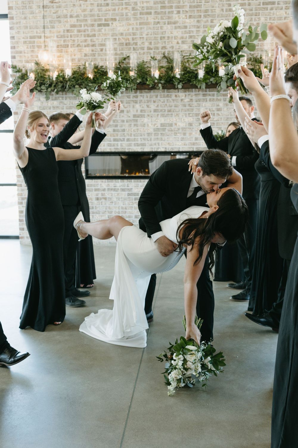Wedding party celebrates as newlyweds share romantic dip kiss.