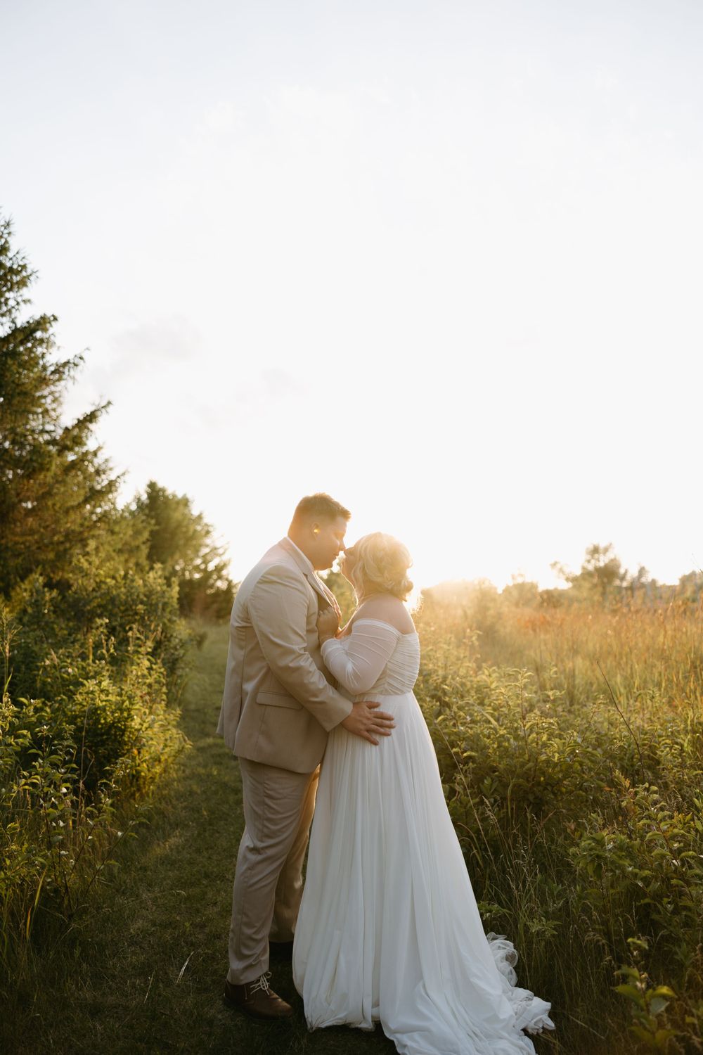 Couple shares romantic moment in field at sunset with golden light.