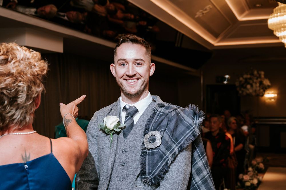 A lively crowd dances and celebrates at an indoor wedding reception with warm lighting and festive atmosphere.