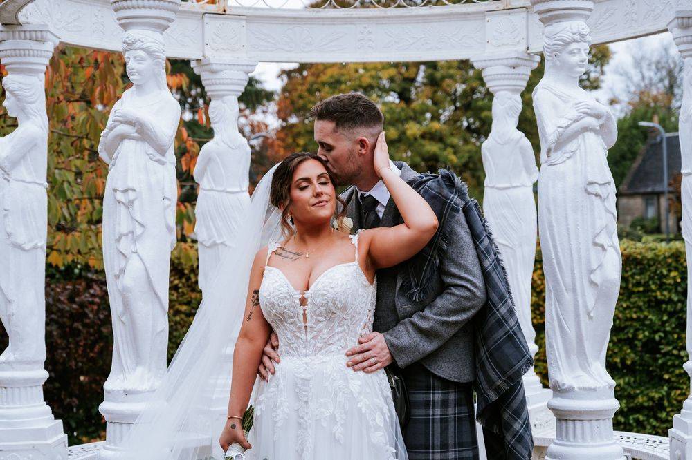 Wedding ceremony setup featuring classical white pillars and statues in a beautiful garden with fall colors.