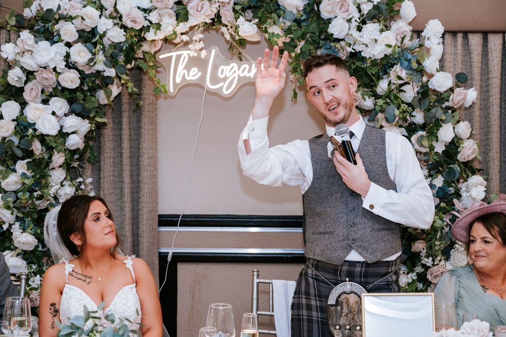 Wedding reception dance floor filled with guests celebrating under elegant white floral arrangements and neon signage.