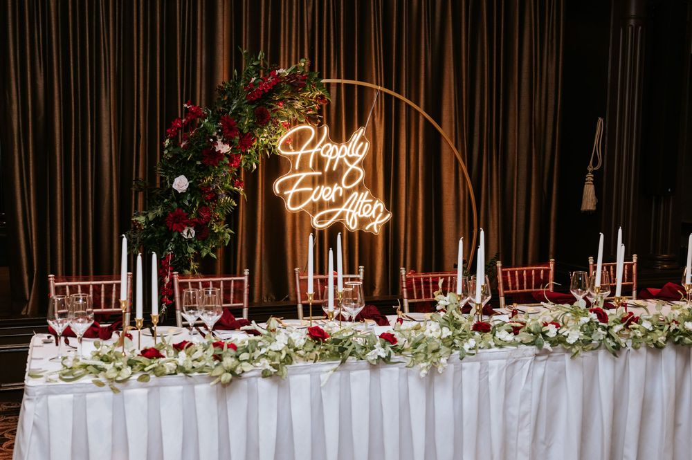Elegant wedding reception table with floral centerpieces and neon signage against a dark backdrop.