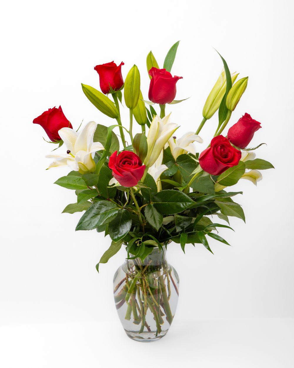 Product photography image of flower arrangement containing red roses and white lilies in a glass vase.