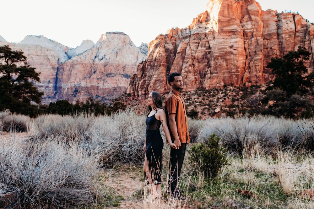 Two figures stand together against stunning red cliffs of Zion National Park at sunset.