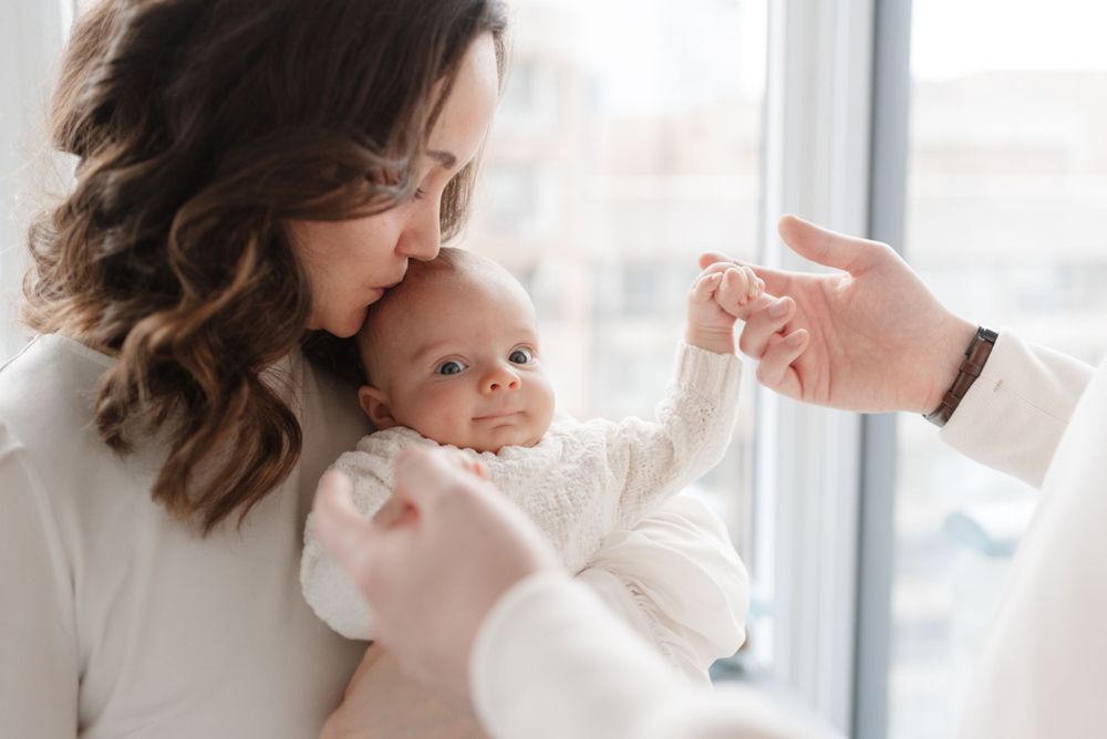 Mom kissing newborn baby for a lifestyle family photoshoot in downtown Toronto, captured by Jess GC Photography in a light candid style